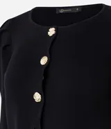 Cardigan de punto negro con cuello redondo, mangas largas abullonadas y cierre frontal con botones decorativos en forma de flor dorada. Presenta un corte corto y ajustado.