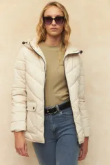 Campera puffer color crudo, con capucha, cierre frontal, bolsillos con solapa y cintura elastizada.