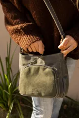 Cartera bandolera de cuero gris con bolsillo frontal exterior de gamuza verde militar con cierre y logo grabado de la marca "Del Sur". Cuenta con correa ajustable para llevar al hombro o cruzada.