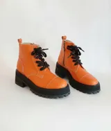 Borcego de cuero color naranja de caña media, con suela de plataforma y taco grueso negro, cordones oscuros y cierre lateral.