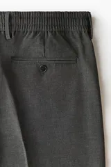 Pantalón de corte relajado en color gris oscuro, con cintura elástica, cierre de botón y cordón de ajuste oculto. Presenta raya marcada en las piernas, bolsillos laterales al bies y bolsillos traseros ribeteados con botón.