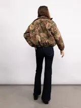 Campera tipo bomber con estampado floral estilo tapicería en tonos oscuros, con cuello clásico, cierre frontal con botones metálicos y bolsillos laterales.