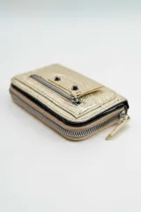 Billetera de cuero sintético plateado con acabado texturizado, diseño con cierre perimetral, bolsillo frontal con cierre y detalle de tachas metálicas.