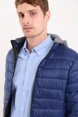 Campera capitoneada color azul marino, con capucha de algodón gris desmontable y cierre frontal. Tiene dos bolsillos exteriores con cierre.