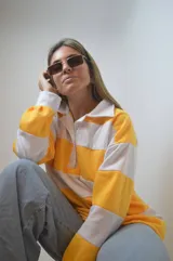 Sweater de punto a rayas horizontales amarillas y blancas, con cuello polo y mangas largas.