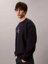Buzo de felpa azul marino con cuello redondo, manga larga y el logo de Calvin Klein estampado en el pecho. Presenta puños, cuello y dobladillo acanalados.