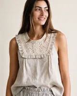 Blusa sin mangas de lino color beige, con pechera artesanal bordada con motivos florales y ribete de volados alrededor del escote y los hombros.