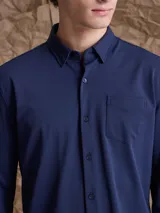 Camisa de manga larga color azul marino, con cuello clásico, cierre frontal de botones y un bolsillo en el pecho.