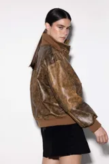 Chaqueta de cuero estilo bomber, con cuello alto, puños y cintura de tejido de punto acanalado. Presenta cierre frontal con cremallera y dos bolsillos laterales con solapa.