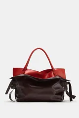 Bolso alargado de piel con doble asa de mano, diseño de doble solapa en combinación de colores y detalle de nudo en los laterales.