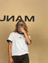 Remera blanca de algodón con cuello redondo y mangas cortas con puños en lurex azul. Tiene un bordado con la letra M en el pecho.