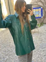 Campera tipo camisa de cuero color verde, con cierre frontal de botones metálicos, cuello clásico y bolsillos frontales con solapa.