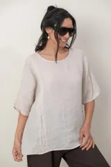 Blusa de lino color marrón oscuro, con escote redondo, mangas cortas amplias y detalle de alforzas verticales en el lateral derecho.