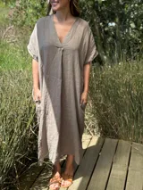 Vestido largo de lino color topo, con escote en V cruzado y mangas cortas amplias. Presenta un corte relajado y bolsillos laterales.