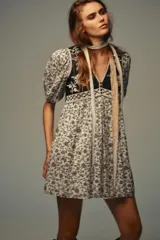 Vestido corto con estampado floral en blanco y negro, escote pico, mangas cortas abullonadas y detalle de chaleco negro con bordados y falsos botones delanteros. Incluye forro interior.