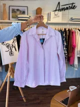 Camisa de corte clásico con estampado de rayas verticales en tonos celeste y blanco. Presenta cuello camisero, cierre frontal de botones y mangas largas con puños con volados.