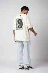 Remera negra de corte oversize confeccionada en tela pesada. Presenta un bordado frontal con la palabra 'REWIND' y un diseño de parche en la espalda con estética de papel roto.