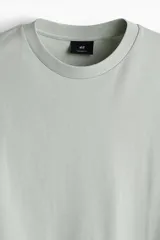 Remera verde claro de algodón pesado, corte oversized, con cuello redondo ribeteado, hombros caídos y bajo recto.