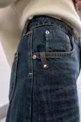 Jeans de tiro medio, color azul oscuro lavado, con corte balloon fit (holgado en muslos y estrechado en el tobillo). Presenta cinco bolsillos, cierre frontal con botones y detalle de trabilla con hebilla en la parte trasera de la cintura.