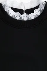 Buzo negro de corte oversized y largo corto, con cuello redondo que presenta un ribete de encaje blanco asomando. Posee hombros caídos y puños y bajo acanalados.