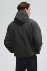 Campera rompevientos de nylon color verde oscuro, con capucha ajustable con cordón, cierre frontal y puños elásticos. Presenta bolsillos laterales y un bolsillo interior, todos con cierre.