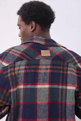 Sobrecamisa de corte holgado con diseño a cuadros en tonos beige y marrón, confeccionada en tejido de textura suave. Presenta cuello clásico, cierre frontal con botones, dos bolsillos con solapa en el pecho y puños abotonados.
