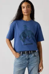 Remera de algodón color azul con estampa frontal de un cowboy montando un caballo, rodeado de pequeños puntos blancos. Presenta cuello redondo y mangas cortas con un corte holgado.