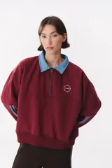 Buzo estilo rugby de corte oversized, color verde oscuro, con cuello tipo camisa en denim azul claro y cierre frontal parcial. Presenta un recorte horizontal en el pecho, logo bordado y tiras laterales en las mangas en contraste.