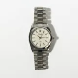 Reloj de pulsera plateado con esfera blanca, agujas negras y correa de eslabones metálicos.