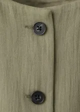 Vestido corto sin mangas color verde militar, con cuello redondo y cierre frontal con botones oscuros. Presenta bolsillos de ribete en la parte delantera y un diseño de corte recto.