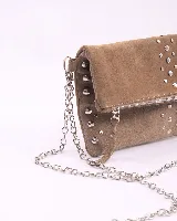 Bandolera de cuero gamuzado color marrón oscuro, con diseño rectangular y solapa frontal decorada con tachas metálicas plateadas. Incluye una cadena metálica plateada larga para usar al hombro o cruzada, y una cadena más corta para llevar como sobre.