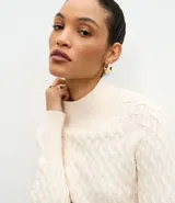 Suéter de punto color crema con textura en zigzag, cuello alto y mangas largas con puños ajustados.