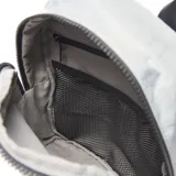 Mochila de nylon color gris, con cierre superior, bolsillo frontal con cierre, bolsillos laterales, manija superior de mano y aplique de cuero sintético con logo grabado en la parte inferior.