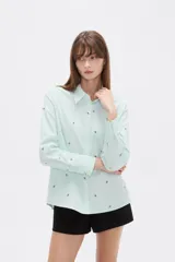 Blusa de corte holgado con cuello camisero y cierre frontal de botones. Presenta un diseño de rayas verticales finas en color azul y blanco, decorado con pequeños bordados dispersos.