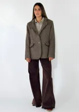 Blazer de corte clásico con textura de tejido de punto, color beige con detalles moteados. Presenta solapas tradicionales, cierre frontal de un botón, bolsillos laterales con solapa y bordes con acabado desflecado.