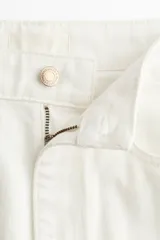 Jean amplio de tiro alto confeccionado en denim rígido color blanco, con diseño de cinco bolsillos y cierre frontal con botón y cremallera.