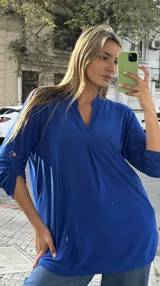 Blusa azul francia de viscosa y lycra, de corte holgado y diseño oversize, con escote en V y cuello estilo túnica. Cuenta con mangas largas con presilla y botón para arremangar.