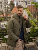 Campera verde militar con capucha, cierre frontal con cremallera y broches, bolsillos laterales con solapa y puños ajustables con velcro.