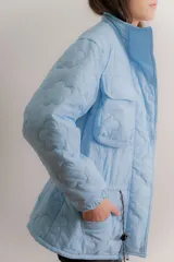 Campera reversible de estilo parka, color celeste, con diseño capitoneado con patrón de flores. Presenta ajuste elástico en la cintura, cuello alto y mangas largas. Incluye parche de marca en la parte superior de la espalda.