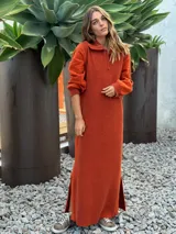 Vestido largo de punto color naranja, con cuello polo y cierre frontal parcial, mangas largas con detalle de calados y tajos laterales en el ruedo.