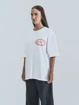 Remera blanca de corte holgado con estampa central en forma ovalada que incluye dragones, estrellas y un ojo, acompañada por el texto 'No Art Uruguay' y 'Castillo de Piria'.