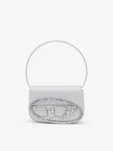 Bolso bandolera Diesel modelo 1DR, color plateado con glitter, con asa corta y correa larga extraíble. Presenta solapa con cierre magnético y logo ovalado "D" metálico en el frente.
