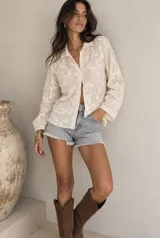 Camisa color manteca de manga larga con cuello camisero, cierre frontal con botones y bordados florales en toda la prenda.