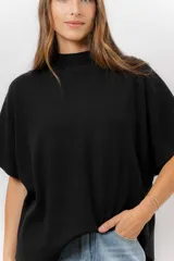 Sweater de tejido de punto color negro, con cuello semi alto y mangas cortas amplias. Presenta una silueta relajada y caída fluida.