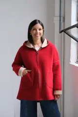 Tapado de paño rojo con capucha, cierre frontal y detalles en color beige en el interior, puños y bordes de los bolsillos. Presenta un corte recto y holgado.
