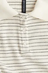 Remera polo de punto acanalado, color crema con finas rayas horizontales negras. Es de manga corta, corte entallado y cuello clásico con tapeta de botones.