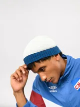 Gorro tipo beanie de punto acanalado en color azul marino, con vuelta en color rojo y blanco a rayas. Incluye etiqueta lateral con el logo de Umbro y el escudo del Club Nacional de Football.