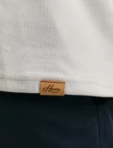 Remera de manga larga con cuello polo, confeccionada en tejido de punto canalé francés. Presenta abotonadura frontal con botones de madera y detalles a contratono en la cartera y el interior del cuello.