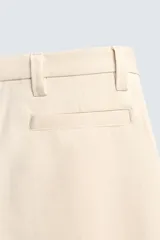 Pantalón chino de corte relajado, confeccionado en tejido estructurado de color beige. Presenta bolsillos frontales, bolsillos traseros de vivo y cierre frontal con cremallera y botón.