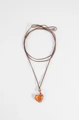 Collar largo con cordón marrón y dije colgante de vidrio en forma de corazón translúcido de color naranja con pequeños puntos decorativos.
